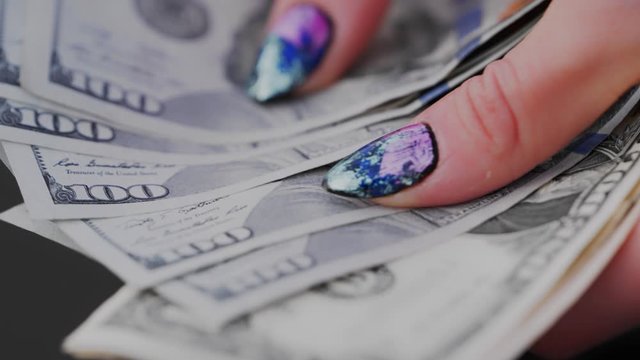 Extreme close up of the female hand with colorful nail polish counting hundreds of dollars. Selective soft focus