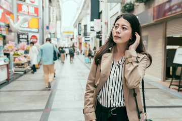 Obraz premium Beautiful elegant young girl with long hair wearing spring coat walking on city street in casual style. lady shopping and buying souvenir in business trip. woman looking curiously in shinsaibashi