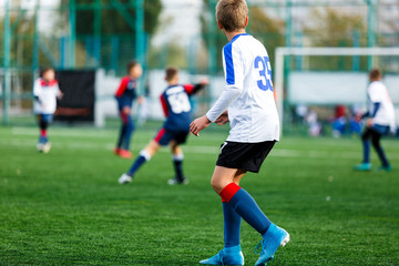 Boys in white and blue sportswear plays football on field, dribbles ball. Young soccer players with ball on green grass. Training, football, active lifestyle for kids concept