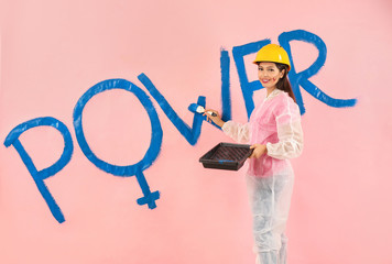 Young woman painting word POWER on color wall. Concept of feminism