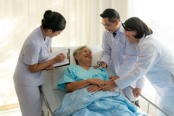Asian medical team of doctors examining and talking to Asian elderly woman patient, health care people take note on clipboard in hospital. Elderly patient care and health lifestyle, medical concept.