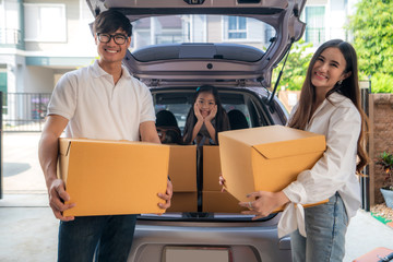 Happy Asian family with father and mother is standing near car with cardboard boxes and their daughter smiling in car at the house garage. Moving day.