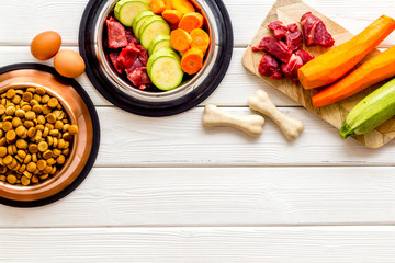 Ingredients of dry feed for dogs - meat, vegetables - near bones on white wooden background top-down copy space