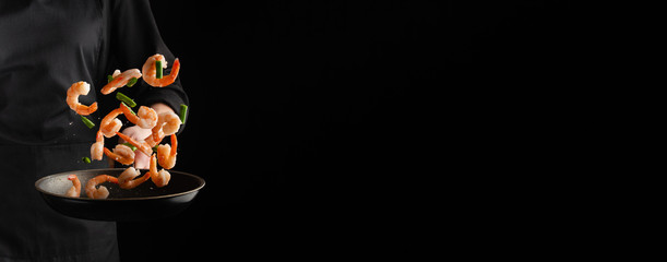 Banner with sea food. The chef cooks shrimps with green beans, freezing in motion. On a black background. Healthy eating.