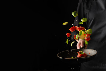 Chef cooks seafood, fries in a pan fresh salmon, trout or tuna with vegetables, Brussels sprouts....
