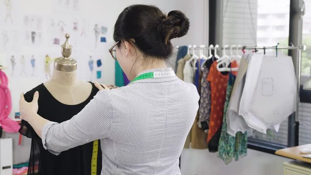 slow motion fashion designer at work in studio alone in start up small business. professional asian woman worker freelance in office holding mannequin turn moving examining checking before customer
