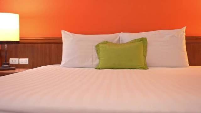 Panning shot from left to right of a empty hotel bedroom with white sheets and pillows and a single green cushion in the middle.