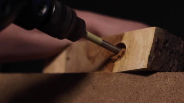 Carpenter using an electric drill to make a hole in a thick slab of a treetrunk that has been smoothed down