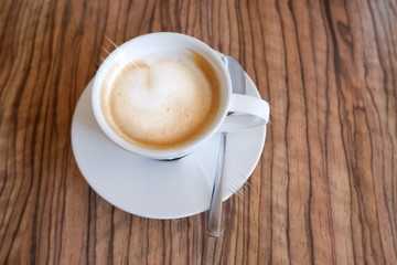 white cup of cappuccino with latte art on wooden background. Beautiful foam, ceramic cup, copy space.hot drink,cappuccino coffee with beautiful latte art on a wooden table background. Morning drinks.