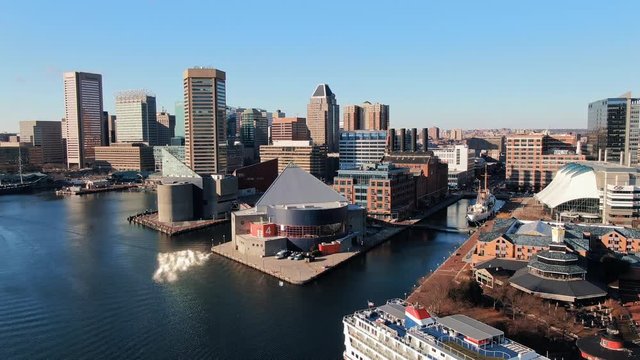 Cinematic rising aerial of Baltimore Inner Harbor skyline including small cruise ship, aquarium, skyscrapers, Chesapeake Bay under blue sky