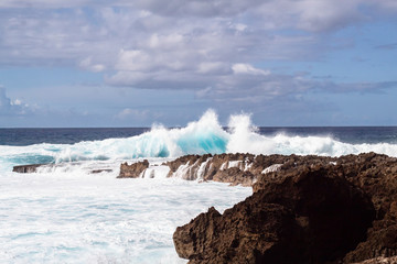 Large waves crashing into the blue ocean with a rocky shore in Hawaii 