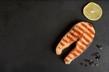 Grilled salmon steak with a pepper and lemon on a slate plate with copy space