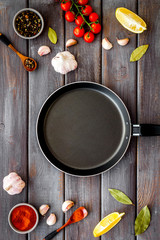 Cooking mockup. Frying pan among spices and vegetables on dark wooden desk top-down copy space