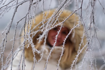 Blurred winter portrait of the young woman among the frosted branches