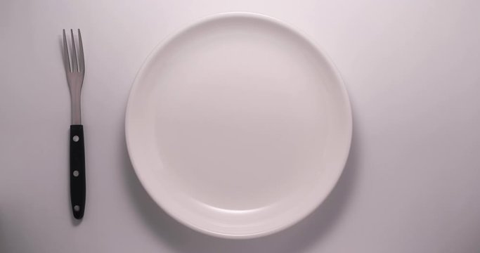 Close up hand put cutlery to an empty white plate on a white background. Dinner place setting. 