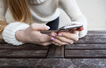 Mobile phone in hand woman in white sweater on wooden table. Close-up, selective focus