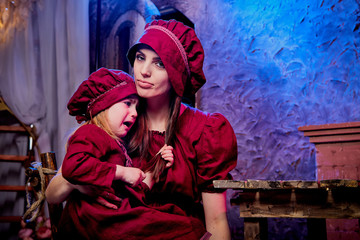 Easter. Family in rural wooden interior with flower in studio. Mother and daughter in maroon or red dresses of the village shepherdesses