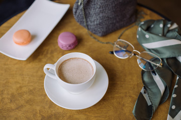 Close up of white cup of hot chocolate, berry macaroons and female accessories on wooden table. Lifestyle concept.