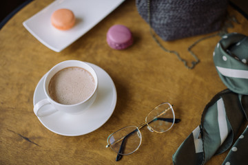 Close up of white cup of hot chocolate, berry macaroons and female accessories on wooden table. Lifestyle concept.