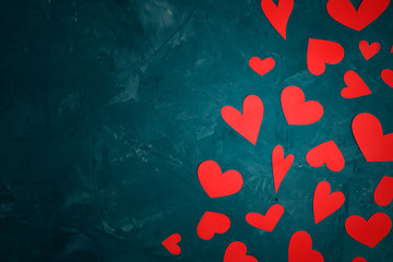 Red hearts of various shapes cut out of paper are scattered on an abstract textured cyan background with copy space.