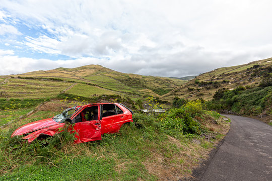 An abandoned smashed red car on the side of the road in rural Flores, Portugal.