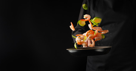 A professional chef cooks shrimp in a pan with brussels sprouts, vegetables. Cooking seafood,...