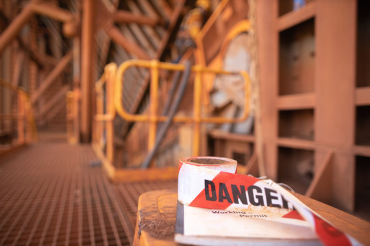 Red and white exclusion dropped zone danger tape tags placing top of working at height permit book and defocused abseiler repairer working in fall restraint fall arrest at the background