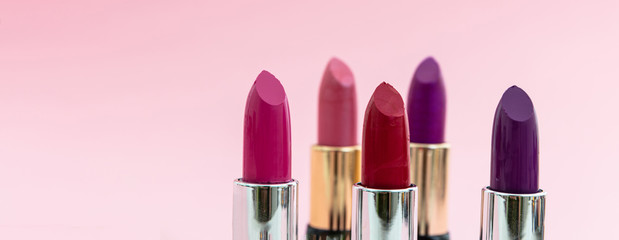 Lipsticks various colors against pink background, closeup view