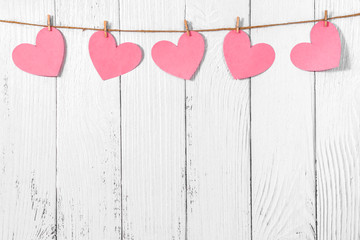 White painted wooden background with a garland of pink hearts. Natural rope and clothespins. Concept of recognition of love, romantic relationships, Valentine's day in grunge style. Copy space