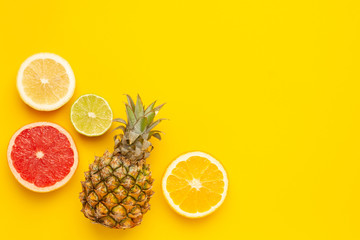 Tropical fruits pineapple, orange and lime on yellow background with copyspace