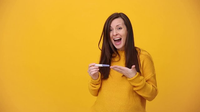 Young woman in bright sweater shirt hold in hands pregnancy test isolated over yellow background in studio. Medical healthcare gynecological, pregnancy fertility maternity people lifestyle concept.