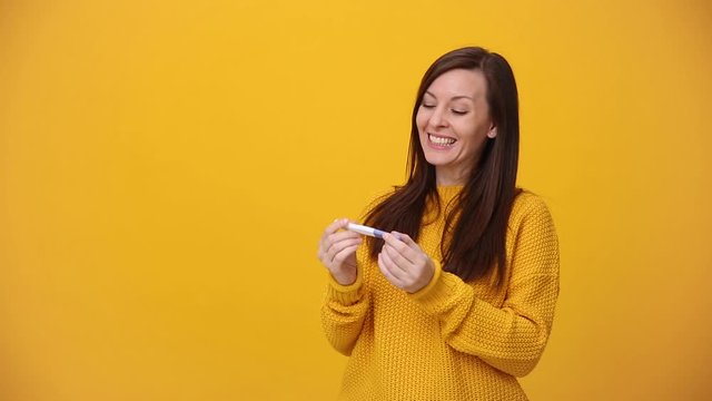 Young woman in bright sweater shirt hold in hands pregnancy test isolated over yellow background in studio. Medical healthcare gynecological, pregnancy fertility maternity people lifestyle concept.