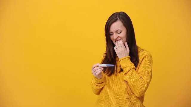 Young woman in bright sweater shirt hold in hands pregnancy test isolated over yellow background in studio. Medical healthcare gynecological, pregnancy fertility maternity people lifestyle concept.