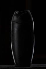 black plastic bottle for shampoo or shower gel on black isolated background
