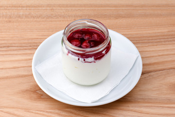 Jelly with berries in glass jar. Italian dessert panna cotta on light wooden table.