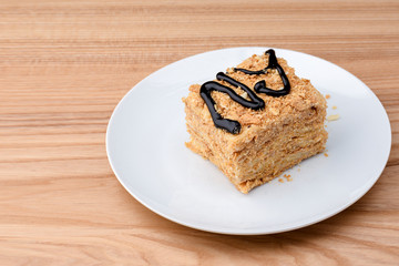Piece of Napoleon cake served on white plate over light wooden table background. Traditional sweet dessert.