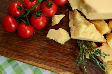 Assortment of cheese parmezan served on wooden cutting board. Cheese with cherry tomatoes and herbs.