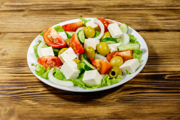Greek salad with fresh vegetables, feta cheese and green olives on wooden table