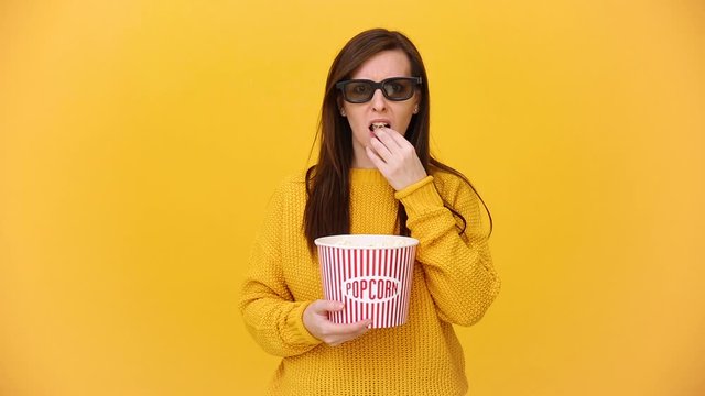 Fun young woman in 3d imax glasses watching movie film, holding bucket, cup of soda, eat popcorn isolated on bright yellow background in studio. People sincere emotions in cinema, lifestyle concept.