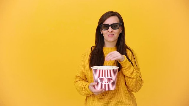 Fun young woman in 3d imax glasses watching movie film, holding bucket, cup of soda, eat popcorn isolated on bright yellow background in studio. People sincere emotions in cinema, lifestyle concept.
