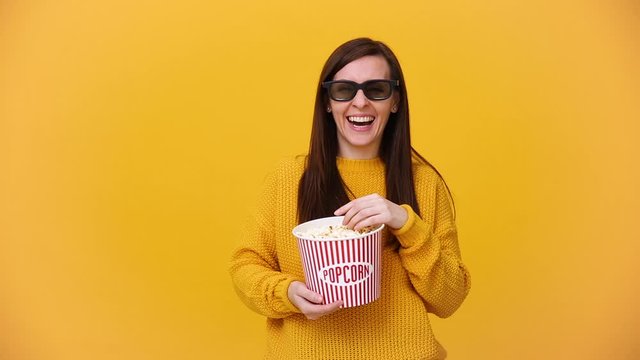 Fun young woman in 3d imax glasses watching movie film, holding bucket, cup of soda, eat popcorn isolated on bright yellow background in studio. People sincere emotions in cinema, lifestyle concept.