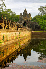Obraz premium Siem Reap, CAMBODIA - gates to Angkor Thom and a bridge with statues of asura demons, ruined antiquity, summer sunny day, reflections in water, horizontal photo