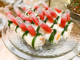 Beautifully decorated catering banquet table with small bites of snacks and appetizers with vegetable role and sauce served on glass plate.