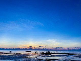 Beautiful, magical sunset, sunrise. Calm sea with boats on the background sky and clouds. Low tide on beach. Blue trend