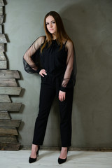 Full-length photo of a pretty brunette girl with excellent make-up in dark clothes standing on a gray background in a luxury vintage interior. The concept of a glamorous portrait.