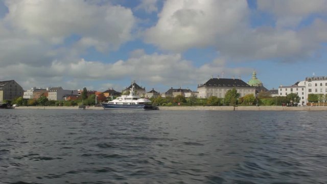 Sunny summer day at the waterfront in Copenhagen, Denmark. Colorful houses facades and farry boat. Floating on the water from right to left.