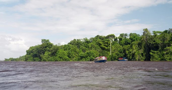 A tourist boat taking visitors on a tour by the shores of Guyana on calm, peaceful waters - Wide shot