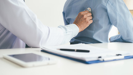 Patient listening intently to a male doctor explaining patient symptoms or asking a question as they discuss paperwork together in a consultation