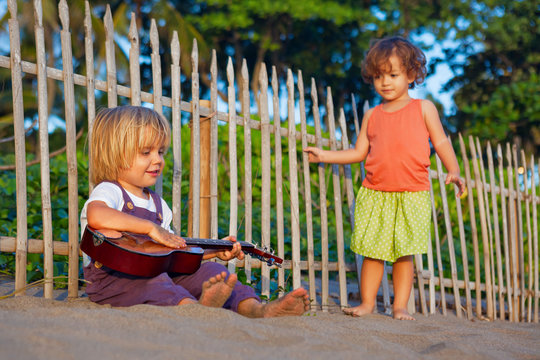 Little happy boy have fun, play music on Hawaiian guitar ukulele for small baby girl, enjoying sunset ocean beach. Children healthy lifestyle. Travel, family activity on tropical island summer holiday