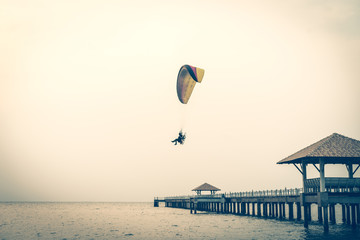 A man is flying with a powered parachute over the beach in Thailand.